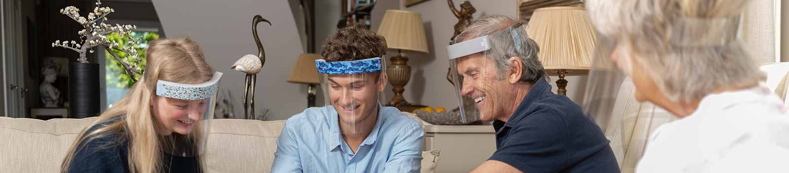 Family of four chatting in a living room wearing the Medworx face visors with a variety of patterned stickers. 